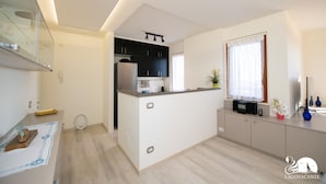 A modern kitchen with a central island, built-in appliances, and a window with curtains. - Appartamento Giada in Padenghe sul Garda (Padenghe sul Garda)