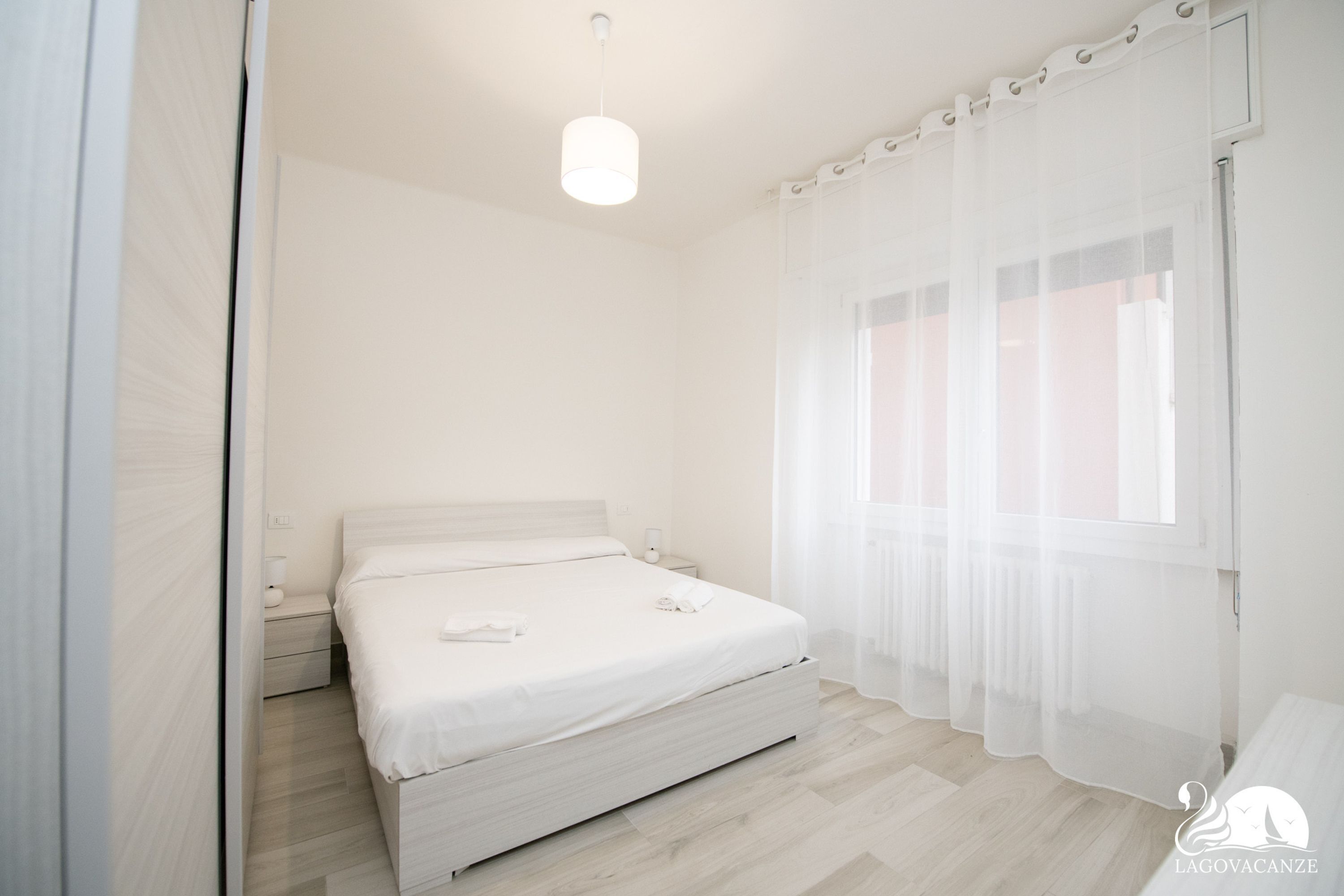 Une chambre à coucher avec un lit, une table de chevet et une fenêtre ornée de rideaux légers.