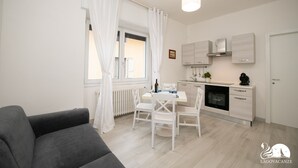 A modern kitchen with white cabinetry, a dining area with a table and chairs, and a grey sofa. - La Torretta - App Catullo (Moniga del Garda)