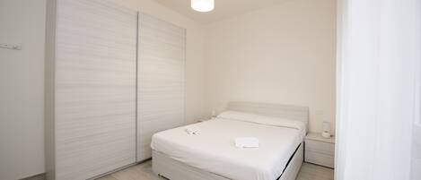 A minimalist bedroom with a bed, bedside table, and a wardrobe.