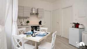A modern kitchen with white cabinetry, a dining table set for two, and a compact refrigerator. - La Torretta - App Catullo (Moniga del Garda)