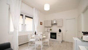 A modern kitchen with white cabinetry, a dining area with a table and chairs, and a large window with curtains. - La Torretta - App Goethe (Moniga del Garda)