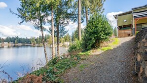 A gravel path leading to a building with a stone wall on one side and a lake in the background. - Cozy, comfortable, peaceful, unique lakeside house w beautiful views/Olympia (Lacey)