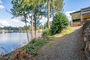 A gravel path leading to a building with a stone wall on one side and a lake in the background.