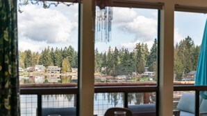 A dining area with a table set for two, overlooking a lake with houses and trees. - Cozy, comfortable, peaceful, unique lakeside house w beautiful views/Olympia (Lacey)