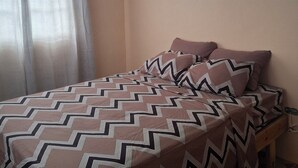 A bedroom with a bed, a ceiling fan, a window with curtains, and a painting on the wall.