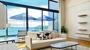 Una habitación moderna con un ventanal grande, un sofá con cojines estampados, una pequeña mesa redonda y una planta.