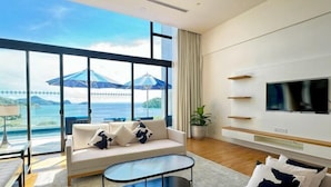 Una sala de estar moderna con un sofá, una mesa de centro, un televisor y ventanas amplias con vista al mar.