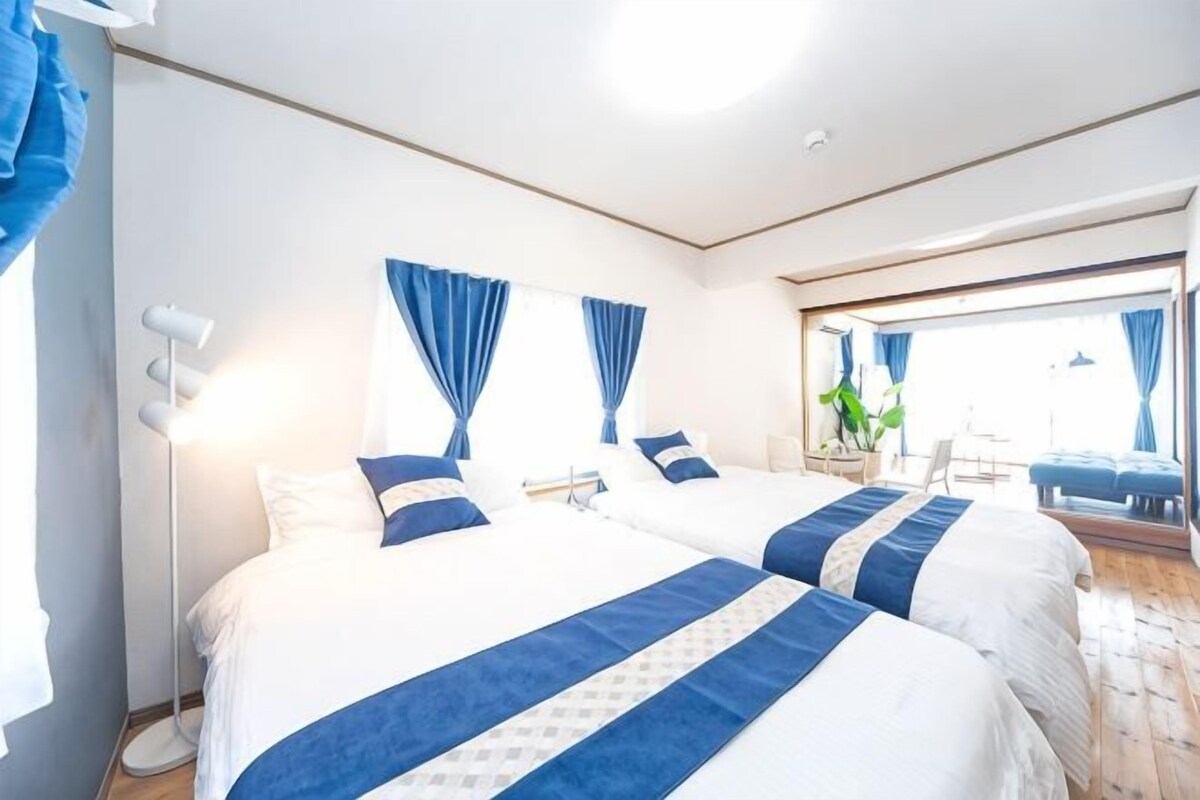 A hotel room with two beds, a large window, a mirror, and a plant.