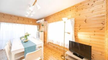 Habitació amb paret de fusta, televisió de pantalla plana, taula de dinar amb cadires i làmpada de peu.