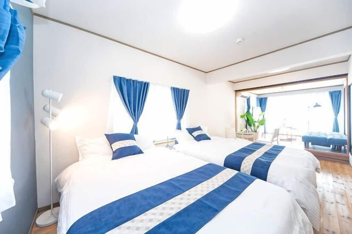 A hotel room with two beds, a large window, a mirror, and a plant.