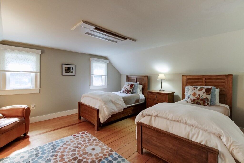 A bedroom with two beds, a wooden floor, a ceiling fan, and a window with blinds.