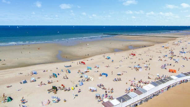 Une vaste plage parsemée de nombreux transats et parasols, un ciel dégagé et l’océan en toile de fond.