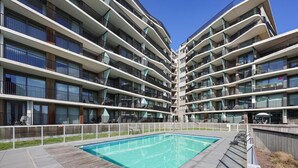 Un immeuble résidentiel moderne à plusieurs étages, doté d’une piscine centrale et d’espaces de détente en plein air.