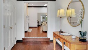 A hallway with wooden flooring, a white rug, a wooden console table with lamps, and a mirror on the wall.