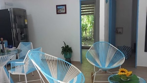 Una sala moderna con sillas azules y blancas, un sillón de balancín de madera, una mesa de comedor y un refrigerador.