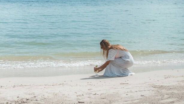 Una mujer con un vestido blanco sentada en la playa cerca del agua.
