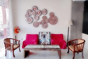 A room with a sofa, two chairs, a coffee table, and a wall with circular wall art. - Seven Hotel (Putatan)