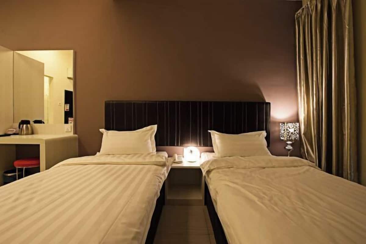 A hotel room with two single beds, a bedside table with a lamp, a mirror, and a desk with a telephone.