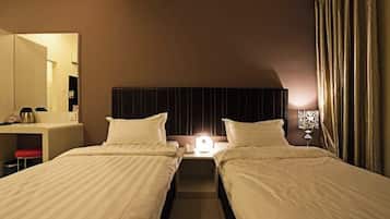 Habitación de hotel con dos camas individuales, una mesita de noche con lámpara, un espejo y un escritorio con teléfono.