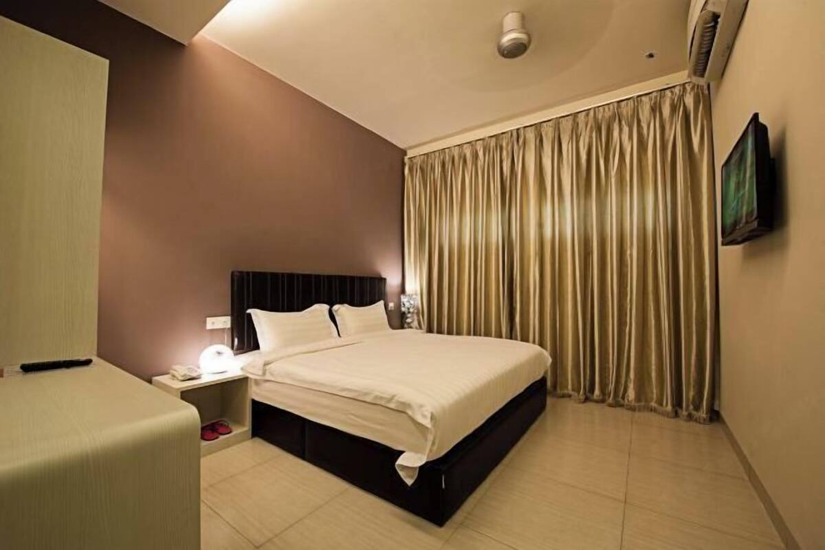 A hotel room with a bed, a nightstand, a TV, and a curtain.
