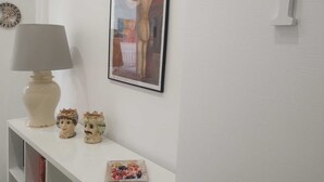Una pared blanca con un cuadro enmarcado, una lámpara y dos figuritas de cerámica sobre una estantería.