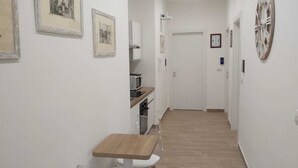 Un pasillo estrecho con una mesa de madera y sillas, un microondas y cuadros en las paredes.