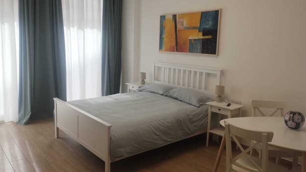 Un dormitorio con una cama, mesitas de noche, una silla, una mesa y un cuadro en la pared.