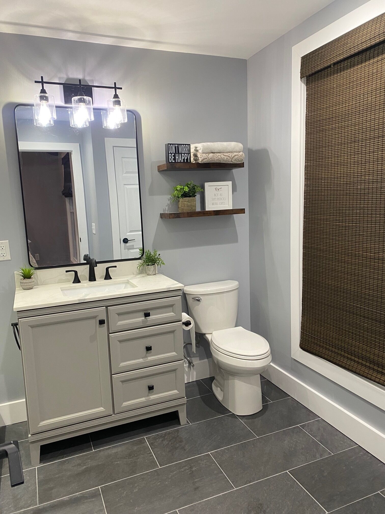 Une salle de bain avec des toilettes blanches, un meuble-lavabo avec un miroir et une étagère avec des serviettes et une plante en pot.