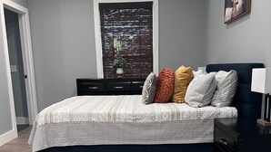 A bedroom with a bed, a nightstand, a lamp, a window with a view, and a door.