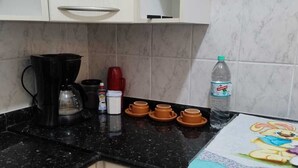 A kitchen with white cabinets, a black countertop, a coffee maker, a red mug, a bottle of water, and a stove with a colorful cloth. - Easy to locate apartment with air conditioning (Itupeva)