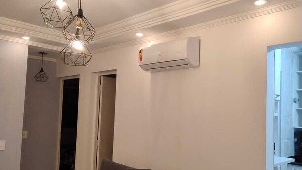 A living room with a grey sofa, pendant lights, an air conditioner, and a kitchen area visible through an open door. - Easy to locate apartment with air conditioning (Itupeva)