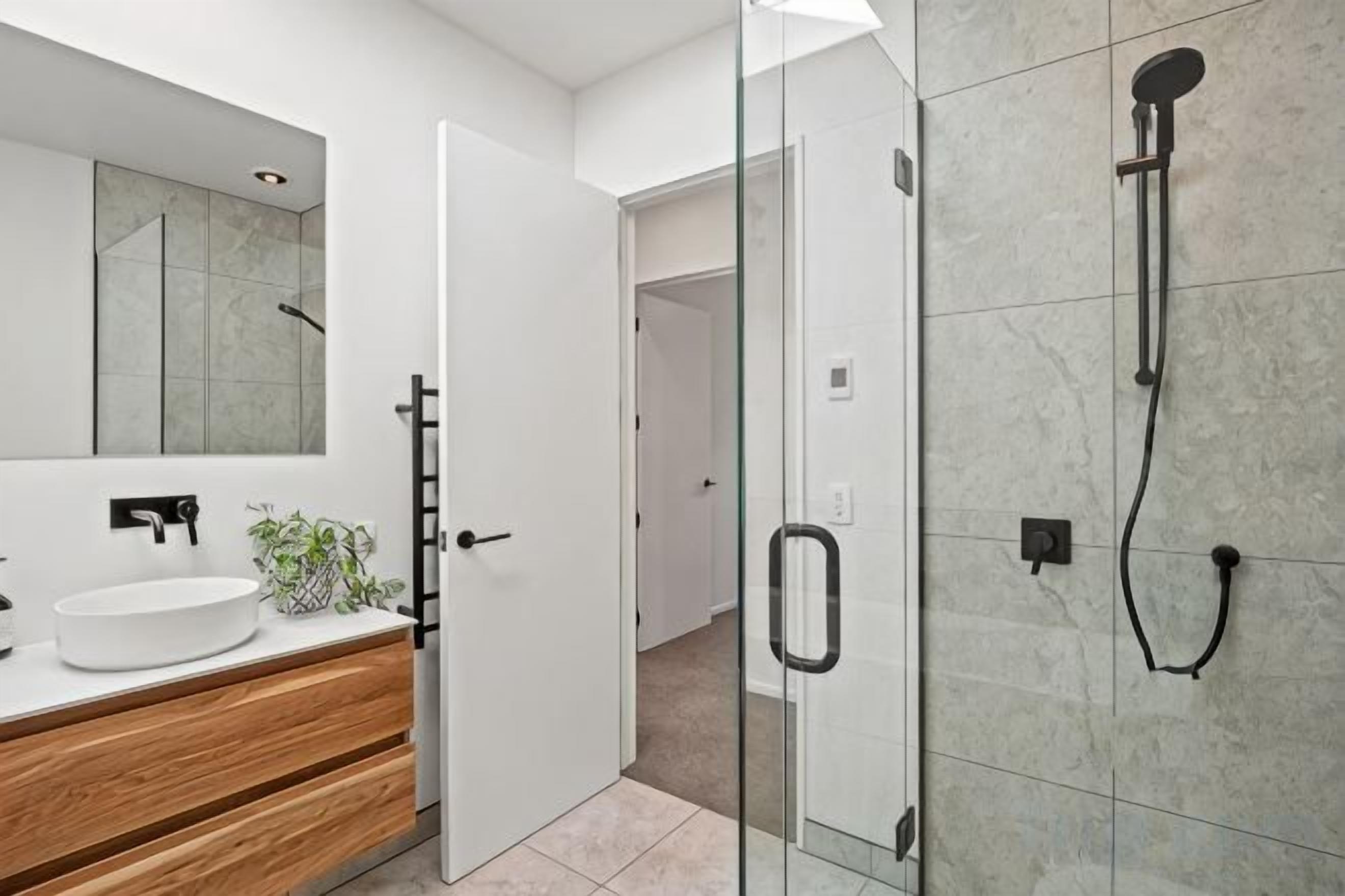 Une salle de bain moderne avec un lavabo blanc, un meuble-lavabo en bois et une cabine de douche en verre.