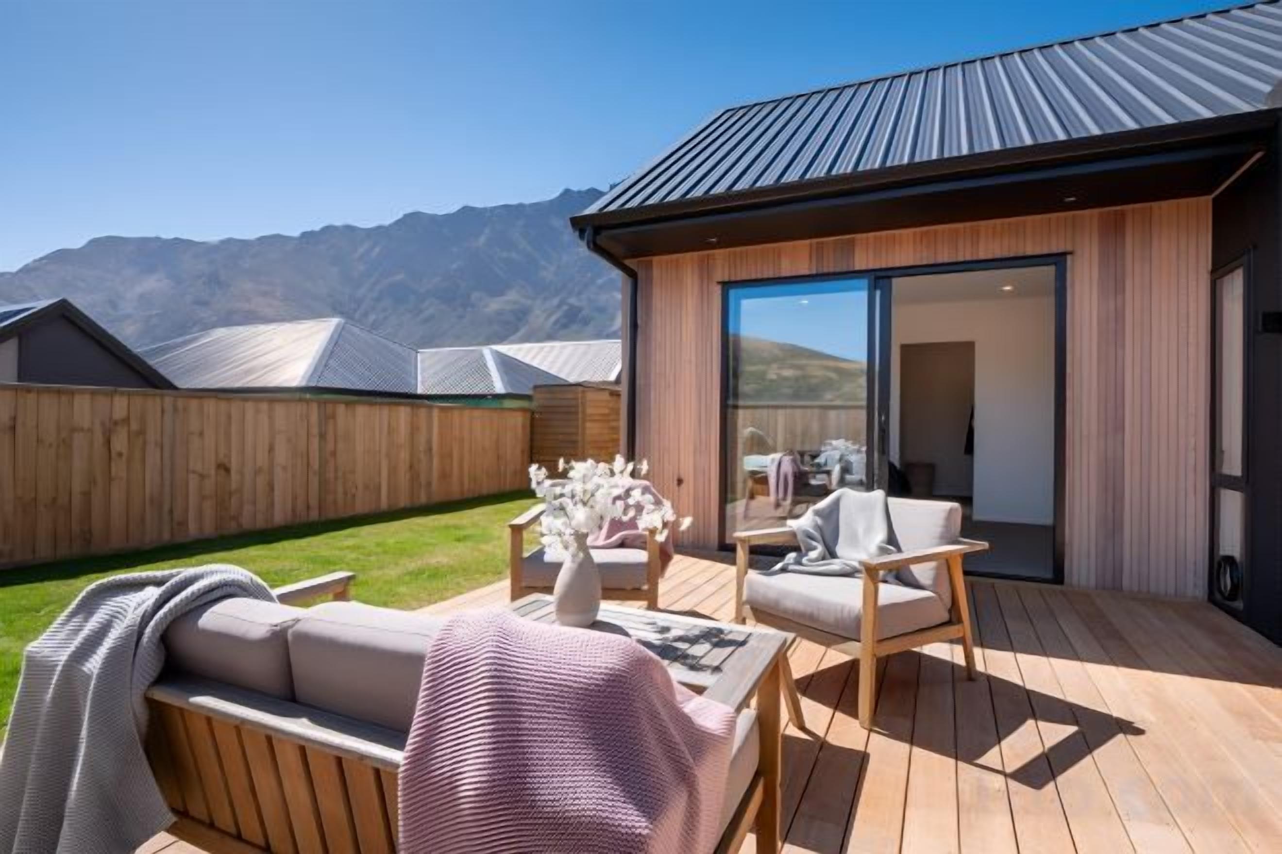 A wooden deck with outdoor furniture, a glass door leading to a room, and a mountain backdrop.