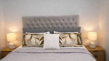 A neatly made bed with a tufted headboard, two bedside lamps, and a floral-patterned pillow.