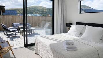 A bedroom with a bed, a balcony with chairs, and a view of the outdoors.