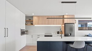 A modern kitchen with white cabinetry, a central island, and a built-in oven. - Remarkable stay in Queenstown (Jacks Point)