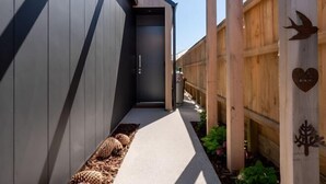 A narrow pathway leading to a building entrance, flanked by wooden fences and decorative metal elements. - Remarkable stay in Queenstown (Jacks Point)