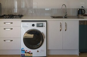 Une cuisine compacte équipée d’un lave-linge intégré, d’un évier et d’une cuisinière.