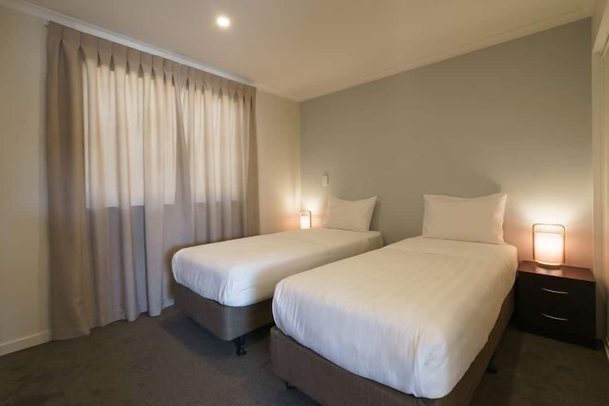 Une chambre d’hôtel avec deux lits simples, une table de chevet avec une lampe et une grande fenêtre avec des rideaux.