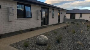 A building with a white brick exterior, large windows, and a paved entrance area with a rock garden. - Jero Apartment (Lake Tekapo)