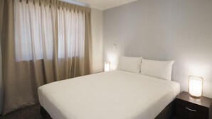 A hotel room with a large bed, a nightstand with a lamp, and a window with curtains. - Jero Apartment (Lake Tekapo)