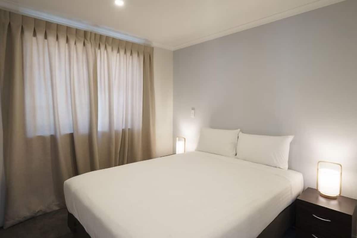 Une chambre d’hôtel avec un grand lit, une table de chevet avec une lampe et une fenêtre avec des rideaux.
