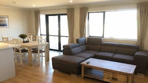 A living room with a sectional sofa, a wooden coffee table, and a dining area with chairs and a table. - Jero Apartment (Lake Tekapo)