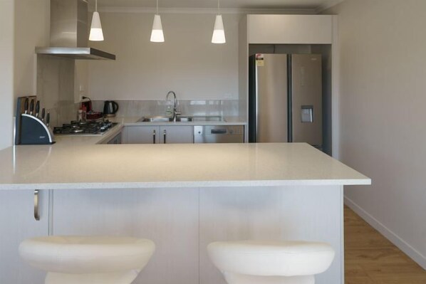 A modern kitchen with a central island, pendant lights, stainless steel appliances, and a built-in oven. - Jero Apartment (Lake Tekapo)