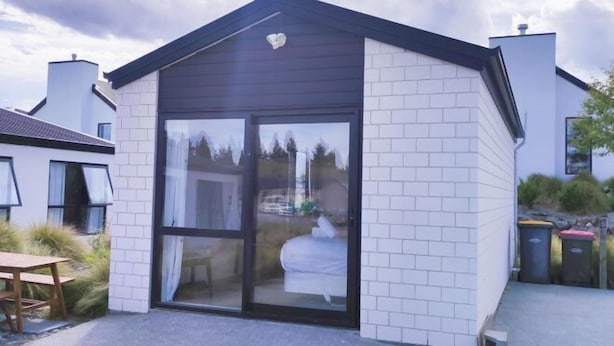 A modern house with a glass door entrance, white brick walls, and a dark roof. - Jero Apartment (Lake Tekapo)
