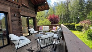 A wooden deck with outdoor seating and a glass door leading to a room. - Le 1853, charming 5* chalet with contemporary interior. Nature, peace and quiet. (Chamonix-Mont-Blanc)