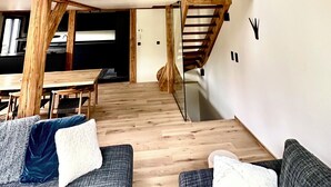 A loft-style living space with exposed wooden beams, a staircase, and a dining area with a table and chairs. - Le 1853, charming 5* chalet with contemporary interior. Nature, peace and quiet. (Chamonix-Mont-Blanc)