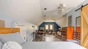 Een slaapkamer met een bed, een plafondventilator, een dressoir en uitzicht op de woonkamer.