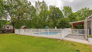 Un jardin avec une piscine, une clôture blanche et un patio couvert.